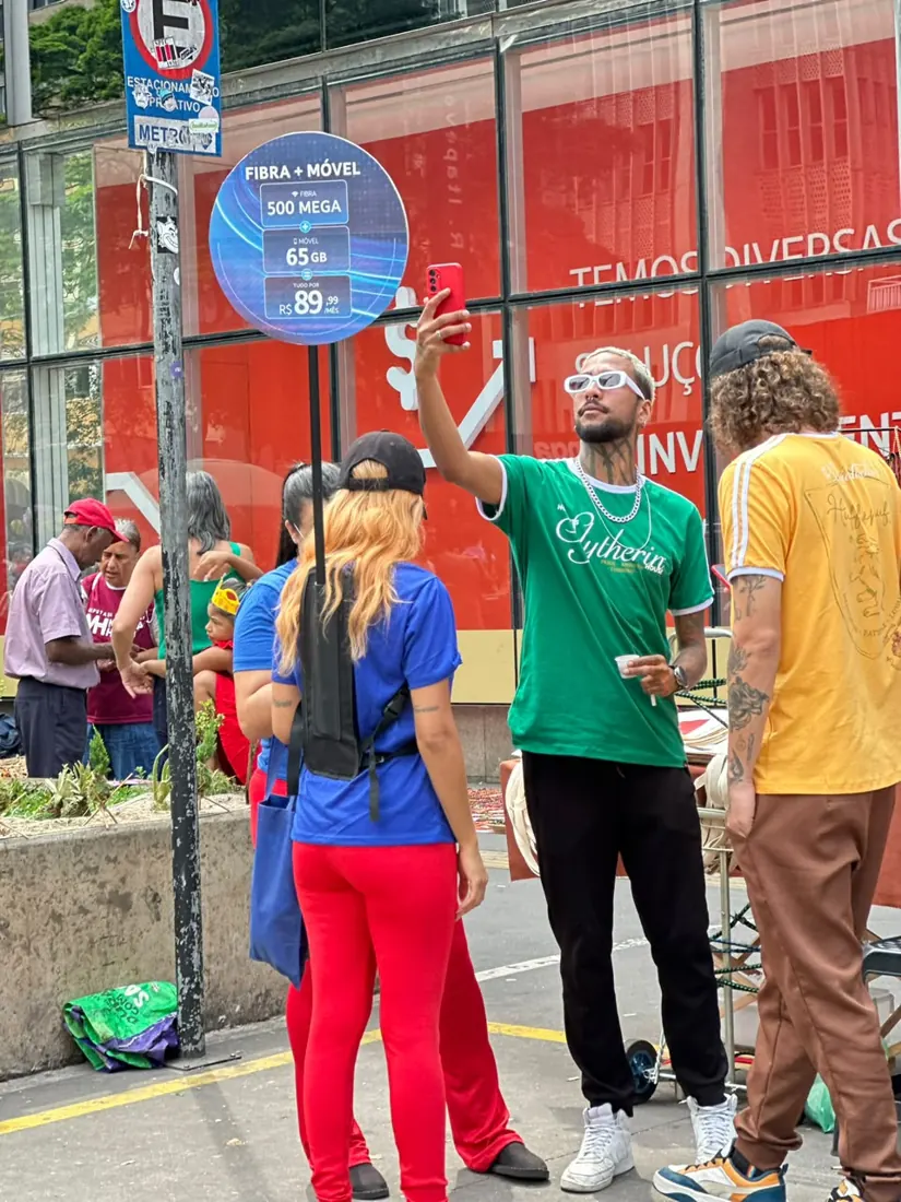 Promotora da TIM abordando um rapaz na Paulista, ao lado da placa Fibra + Móvel